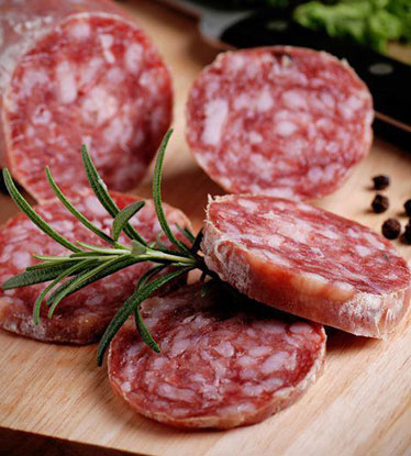 Sliced hard salami on cutting board with sprig of rosemary